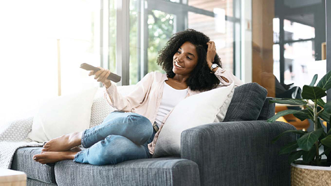 A woman sits on a couch and watches TV.